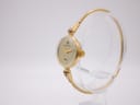 Three-quarter view of the Michel Herbelin watch showing the gold-tone case, cream dial, and integrated bangle bracelet on a clear stand.