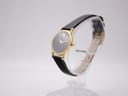 Angled view of the Movado watch on a stand, showing the polished gold-tone case and the black leather strap.