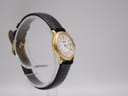 Side view of the Raymond Weil 9972 watch on a clear stand, highlighting the slim profile of the gold plated case and the texture of the black leather strap.