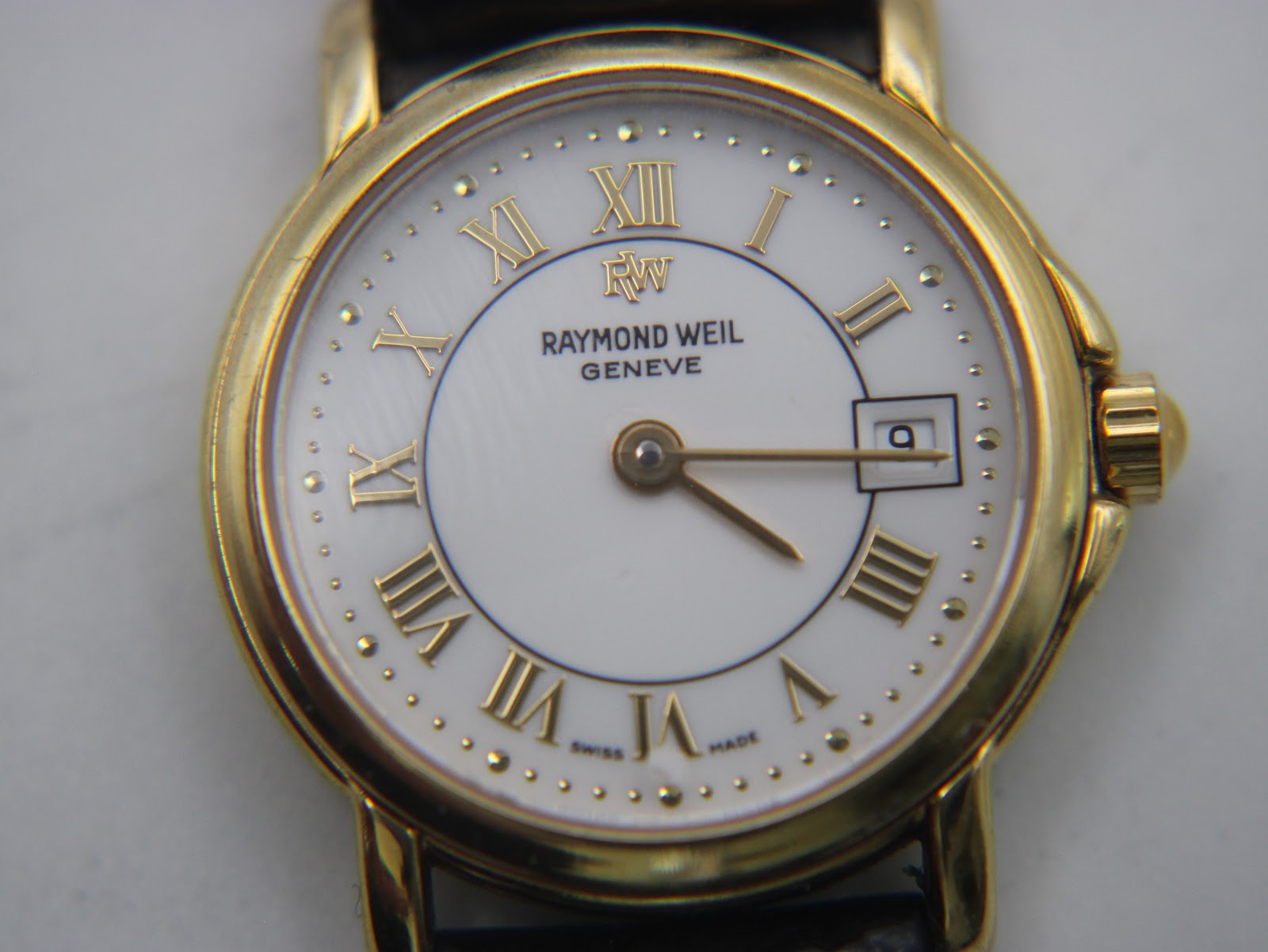 Detailed close-up of the Raymond Weil 9972 white dial with raised gold Roman numerals, dot indices, the RW logo, 'Raymond Weil Genève' text, and a date window at 3 o'clock.