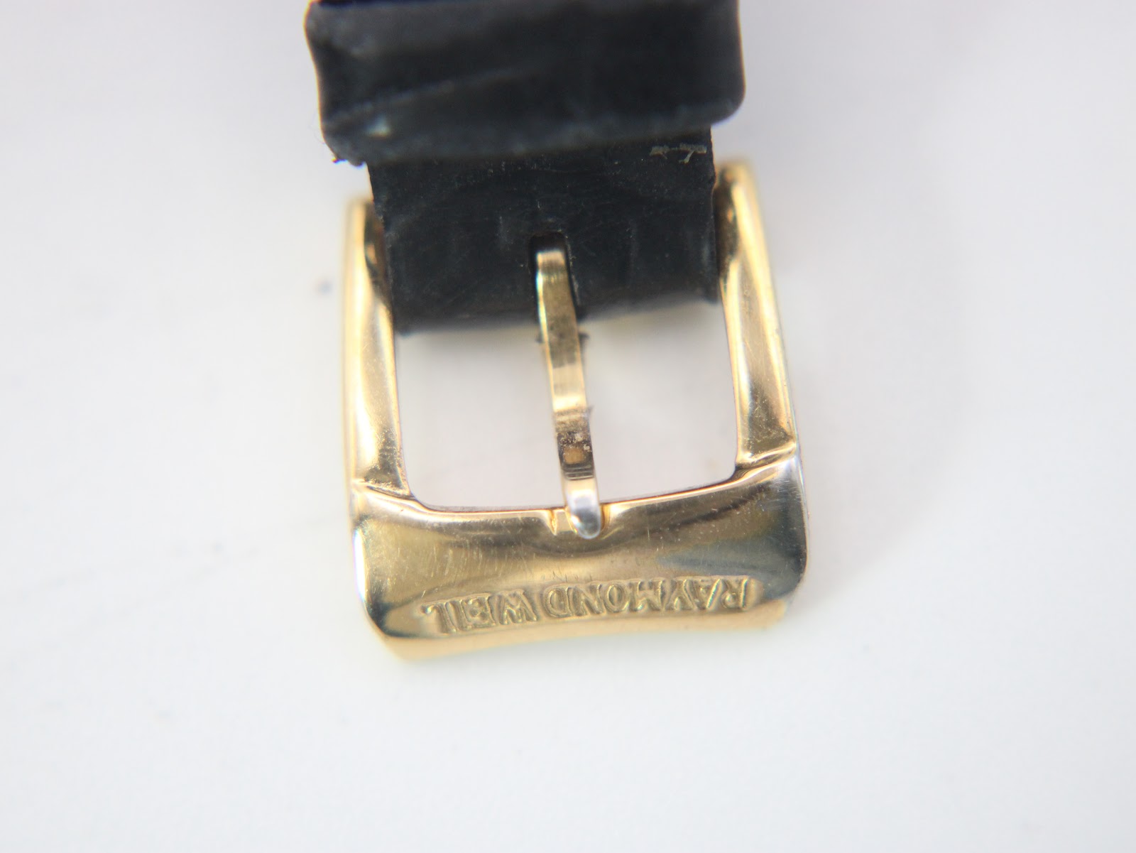 Close-up of the gold plated buckle, clearly showing the "Raymond Weil" signature engraved on it.