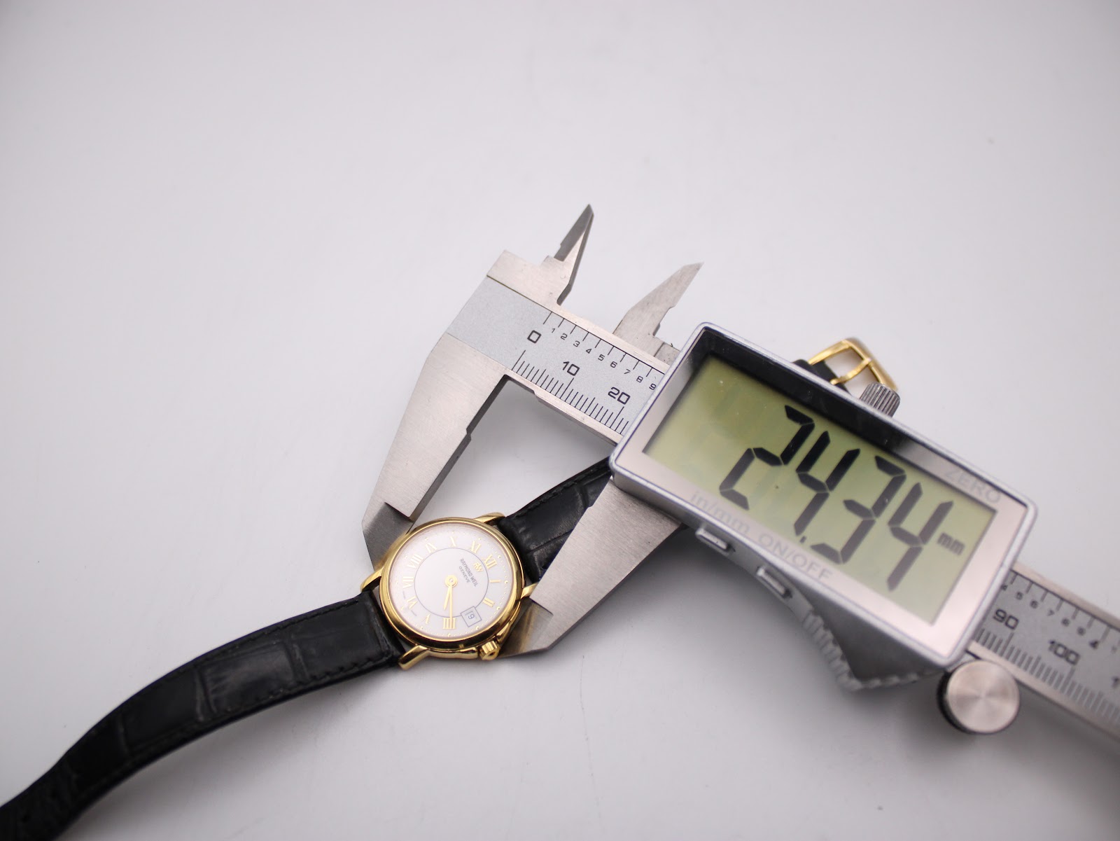 Digital caliper measuring the case diameter of the Raymond Weil 9972 watch, displaying a precise reading of 24.34mm.