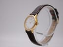 Angled side view of the Tissot C225K watch on a clear stand, highlighting the gold-plated case and crown.