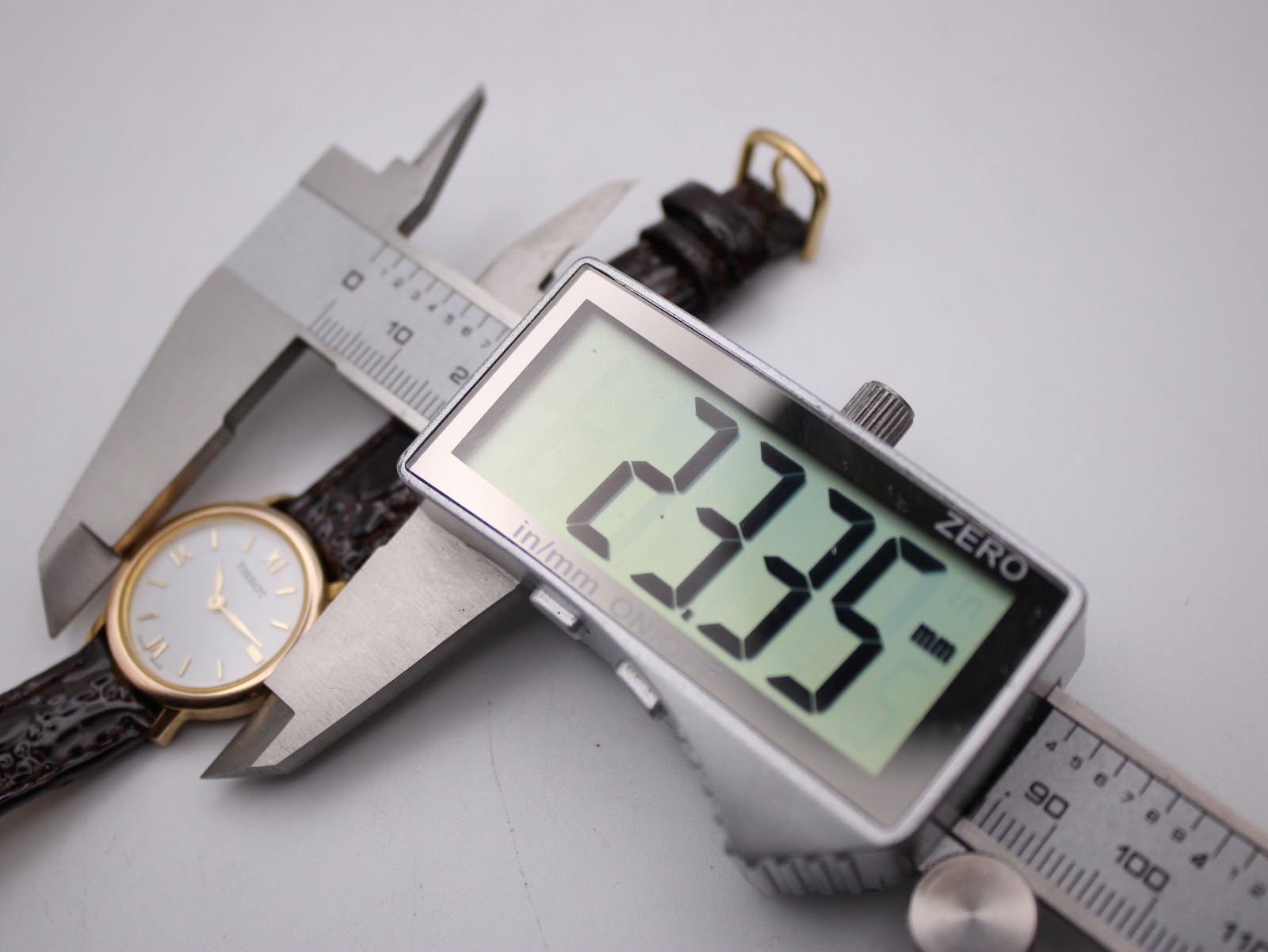 Digital caliper measuring the Tissot watch case, displaying a precise diameter of 23.35mm.