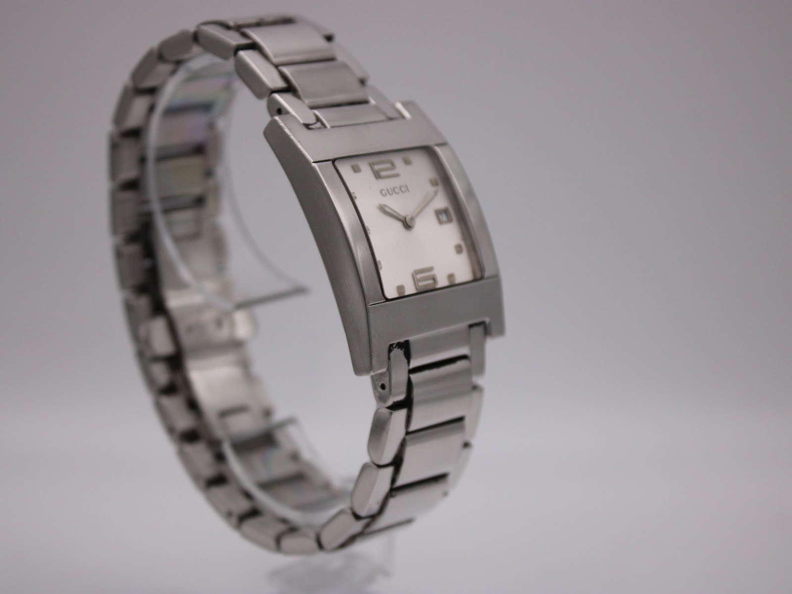 Opposite angled view of the Gucci 7700 M watch on a display stand, highlighting the sleek lines of the square case and bracelet.
