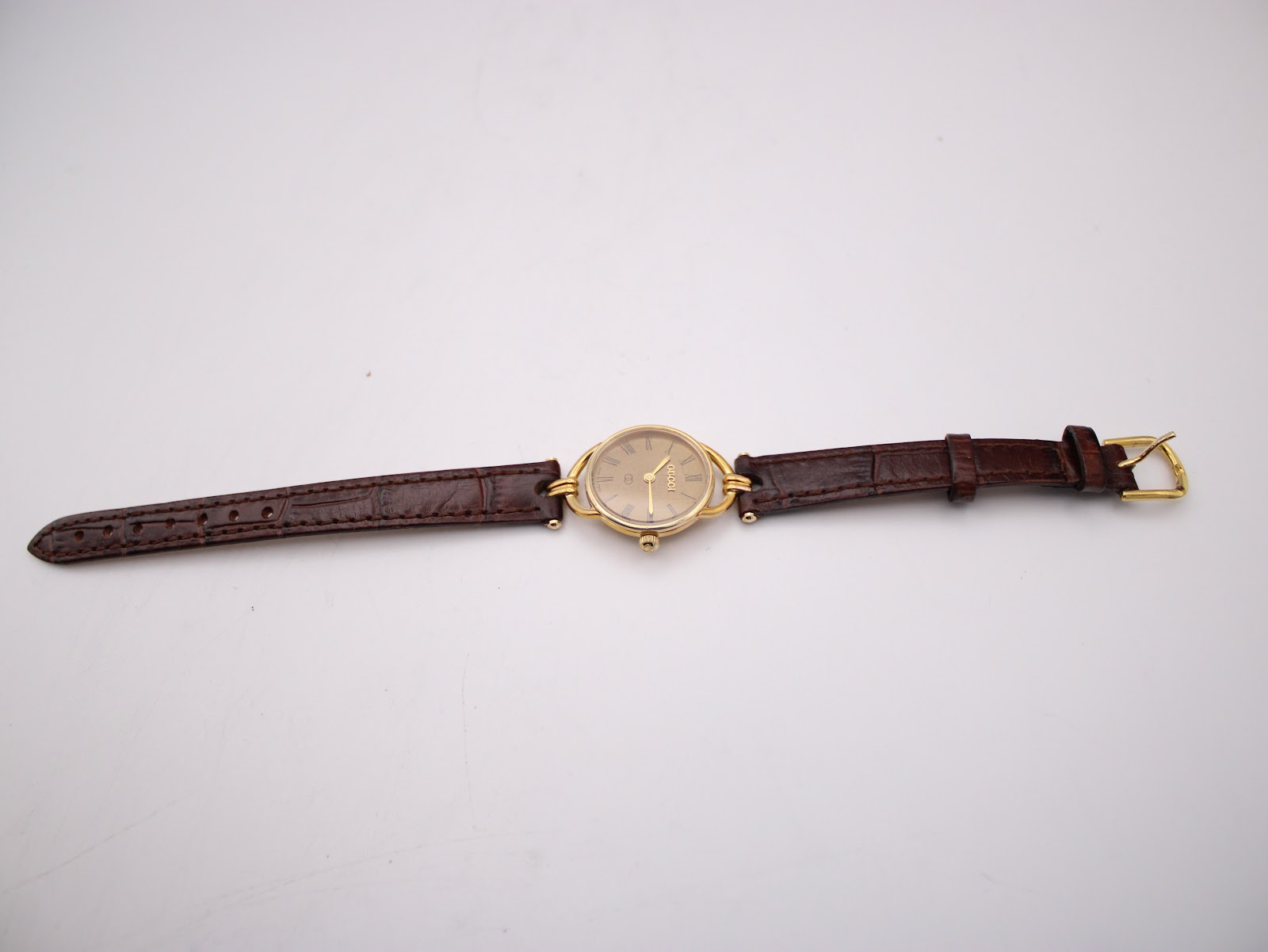 Overhead view of the Gucci 6000L watch laid flat, displaying the full length of the brown leather strap with its gold-tone buckle.