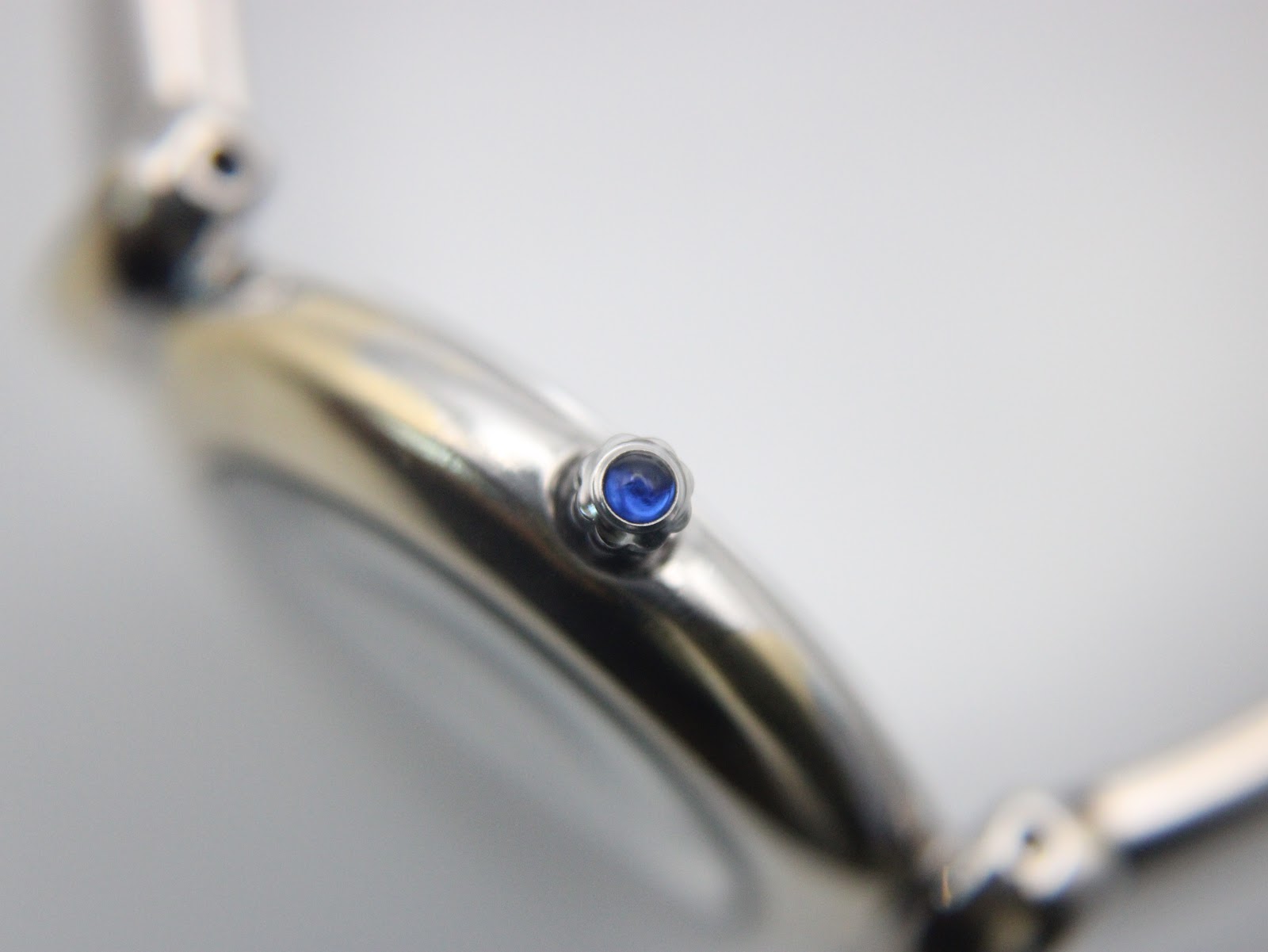 Macro shot of the watch crown, featuring a prominent blue cabochon.