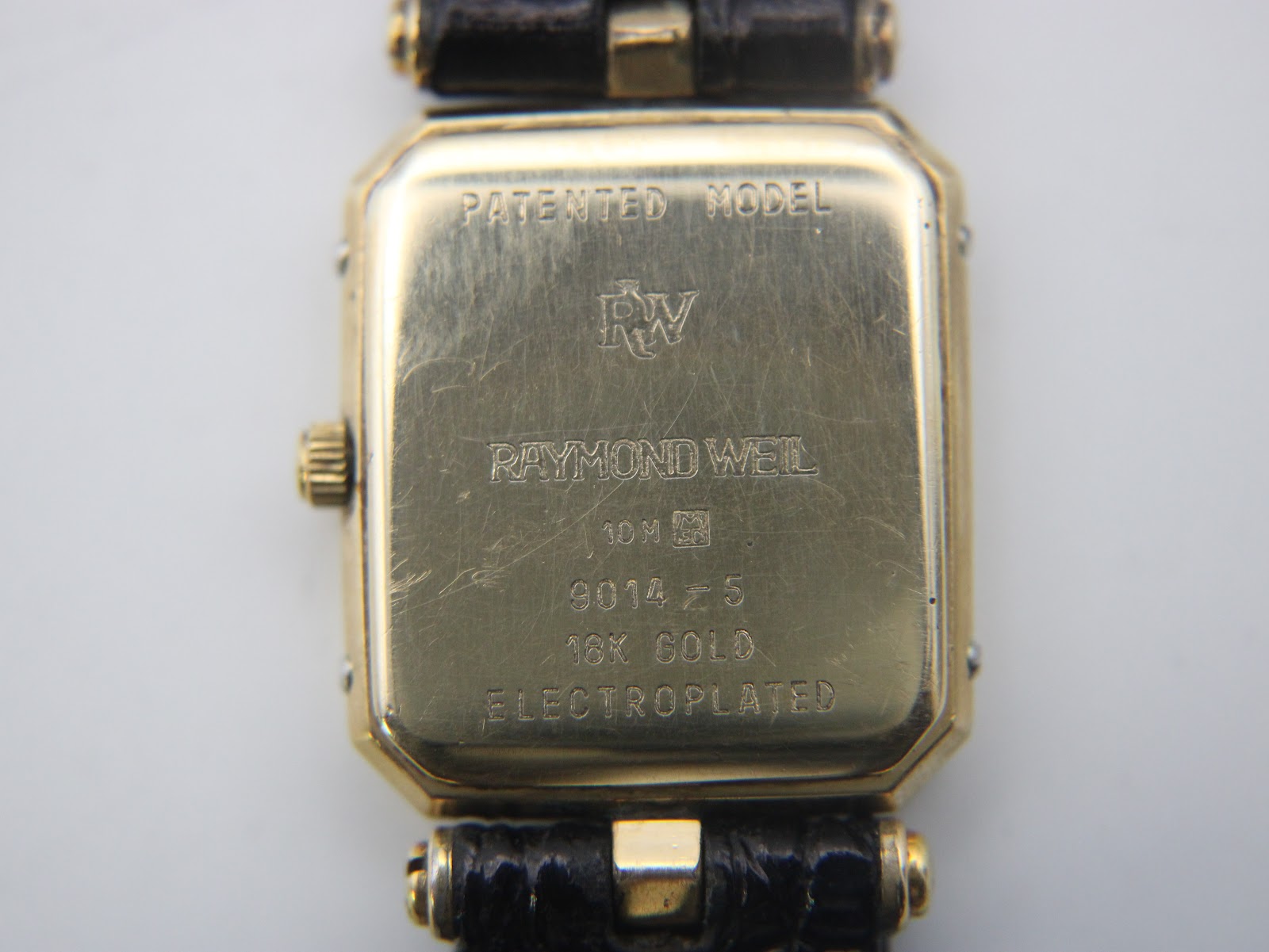 Close-up of the watch case back showing 'PATENTED MODEL', 'RW' logo, 'RAYMOND WEIL', '10M', '9014-5', and '18K GOLD ELECTROPLATED' engravings.