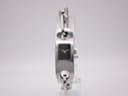 Front view of the Gucci 6100L watch on a clear stand, showing its rectangular case, black dial, and integrated chain-link bracelet.