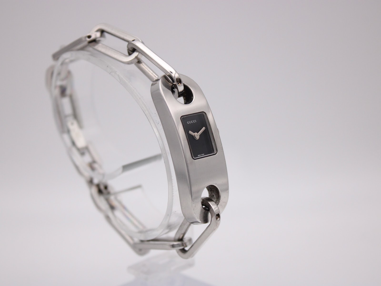 Three-quarter view of the Gucci 6100L, showcasing the overall design of the watch and bracelet on a clear stand.