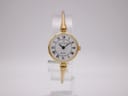 Front view of a Michel Herbelin gold tone bangle watch with a white Roman numeral dial on a clear display stand.