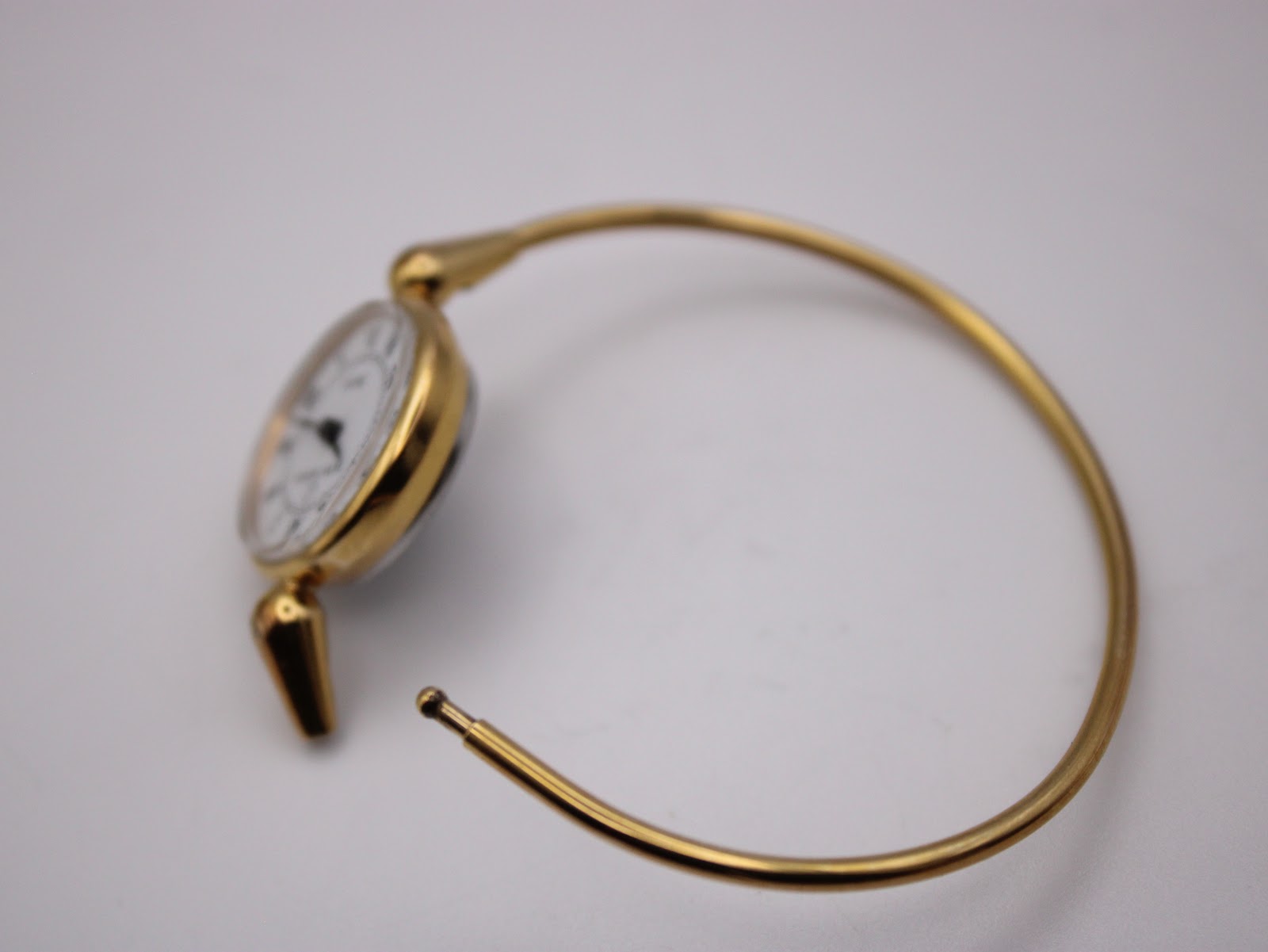 Side view of the open gold tone integrated bangle bracelet, displaying the clasp mechanism.