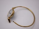 Side view of the open gold tone integrated bangle bracelet, displaying the clasp mechanism.