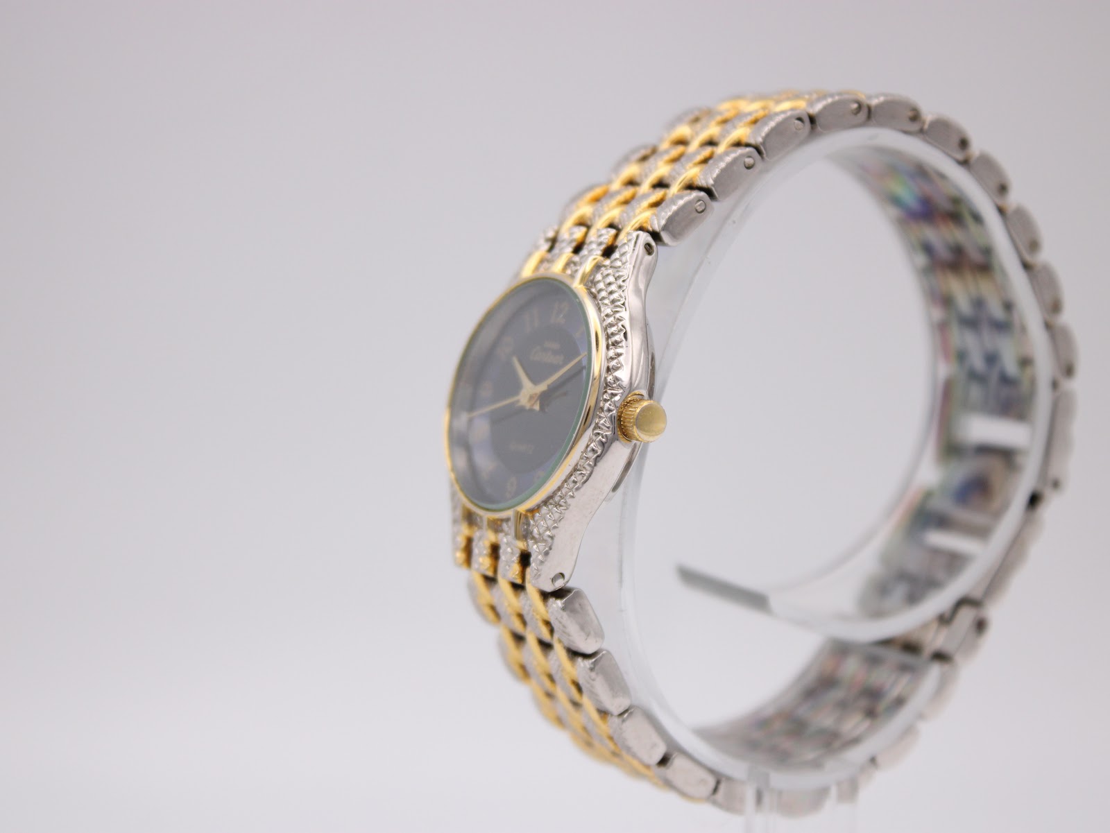 Side view of the Manin Cartear watch on a stand, showing the textured bezel and gold crown.