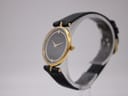Angled side view of the Raymond Rone watch on a clear stand, highlighting its slim profile and gold-plated case.