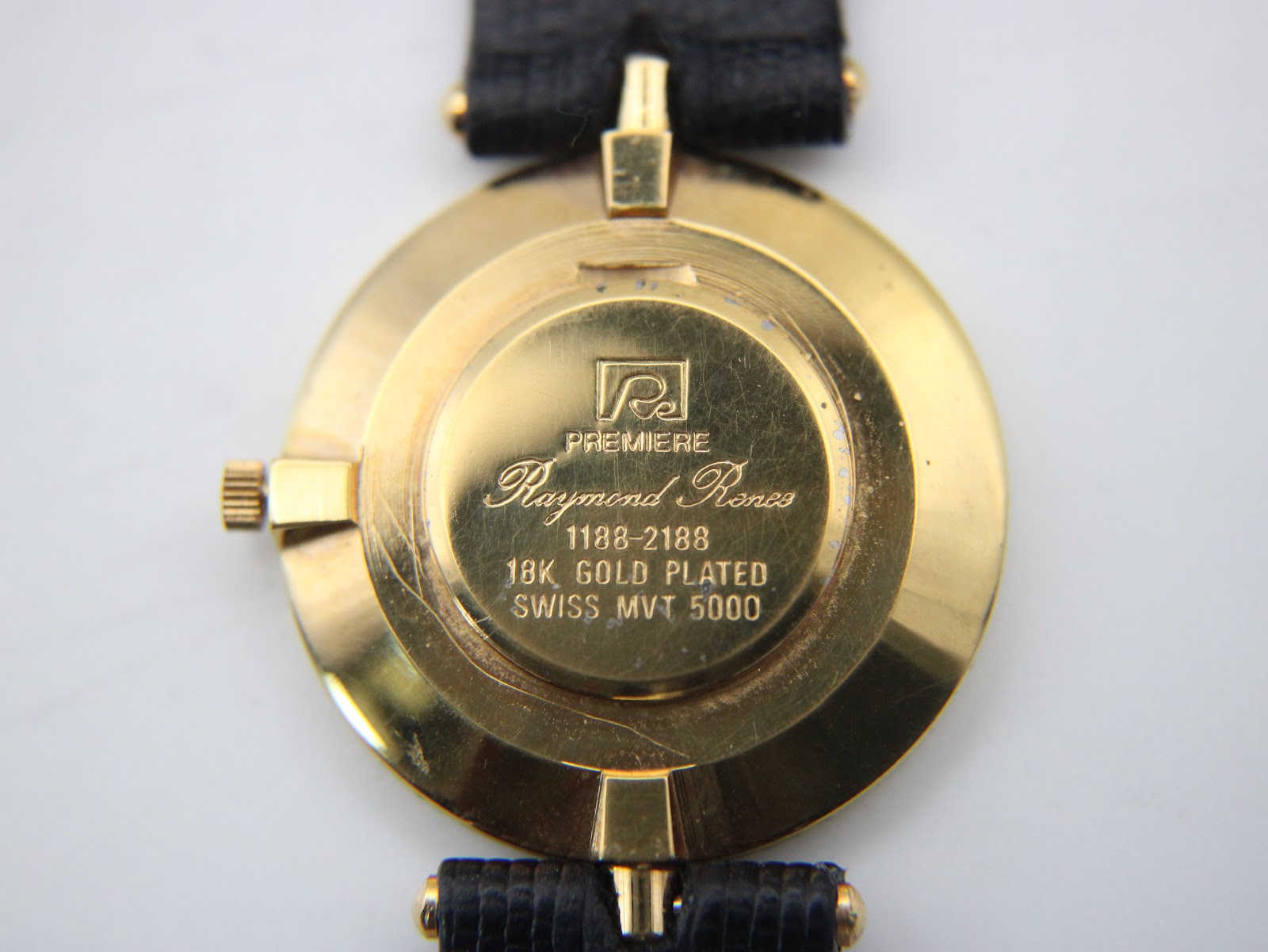 Close-up of the watch case back, showing 'Premiere', 'Raymond Rone', '1188-2188', '18K GOLD PLATED', and 'SWISS MVT 5000' engravings.
