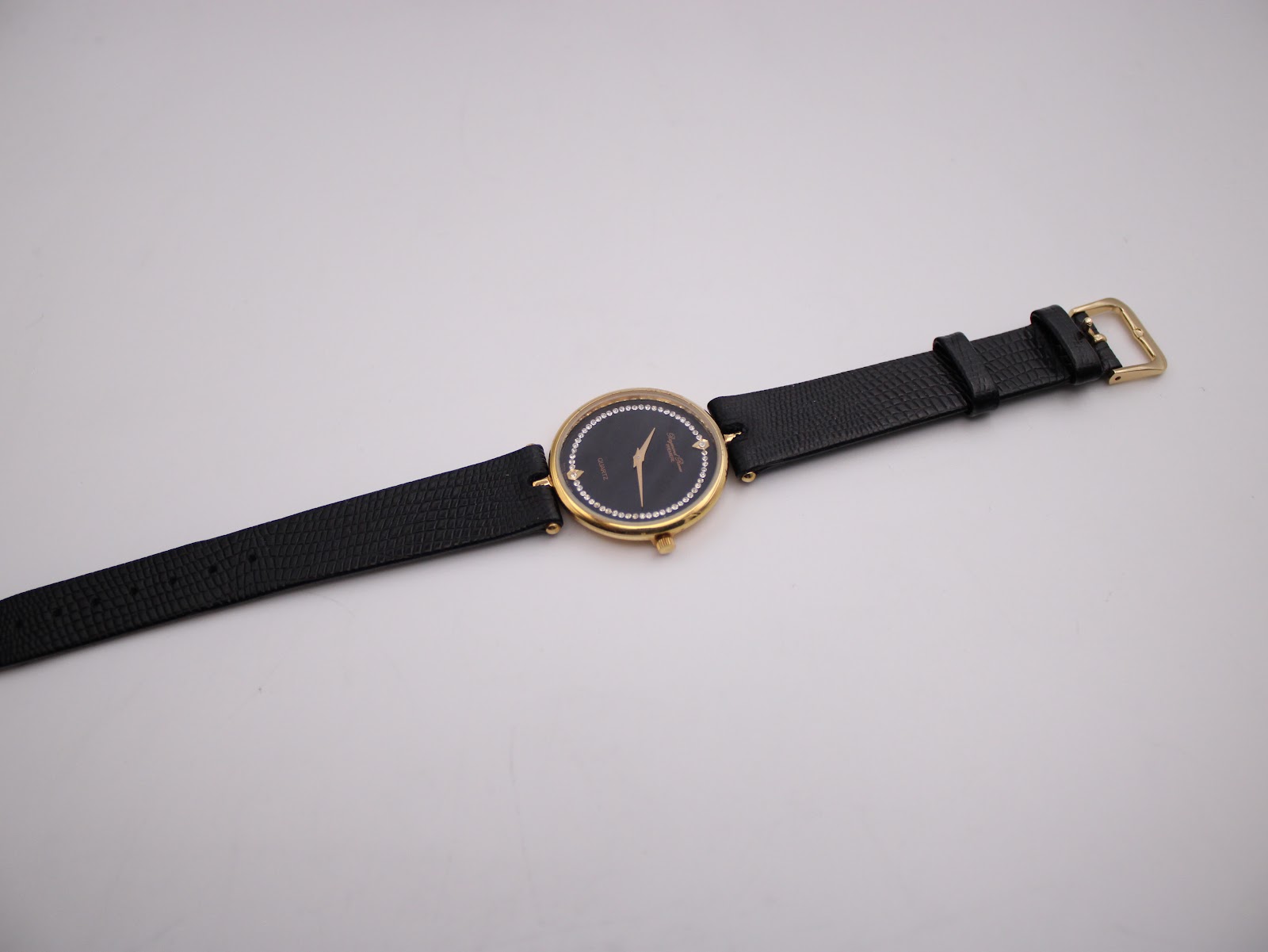 Full length view of the Raymond Rone watch laid flat, displaying the black leather strap and gold-tone buckle.