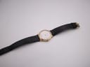 Full view of the Raymond Weil watch and black leather strap stretched out on a white surface.