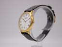 Angled side view of the Jean Perret QJ watch on a stand, highlighting the gold-tone case and brown leather strap.