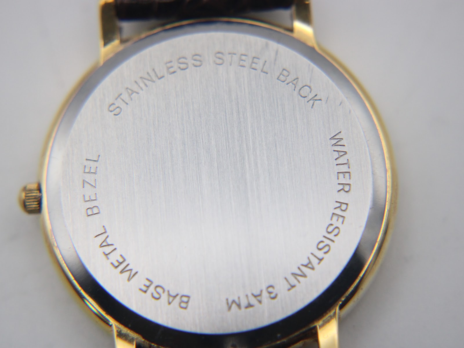 Close-up of the watch's stainless steel case back with engravings 'STAINLESS STEEL BACK', 'BASE METAL BEZEL', and 'WATER RESISTANT 3ATM'.
