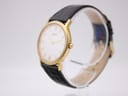 Angled view of the Tissot watch showing the gold-tone case, white dial, and crown, with the strap on a stand.