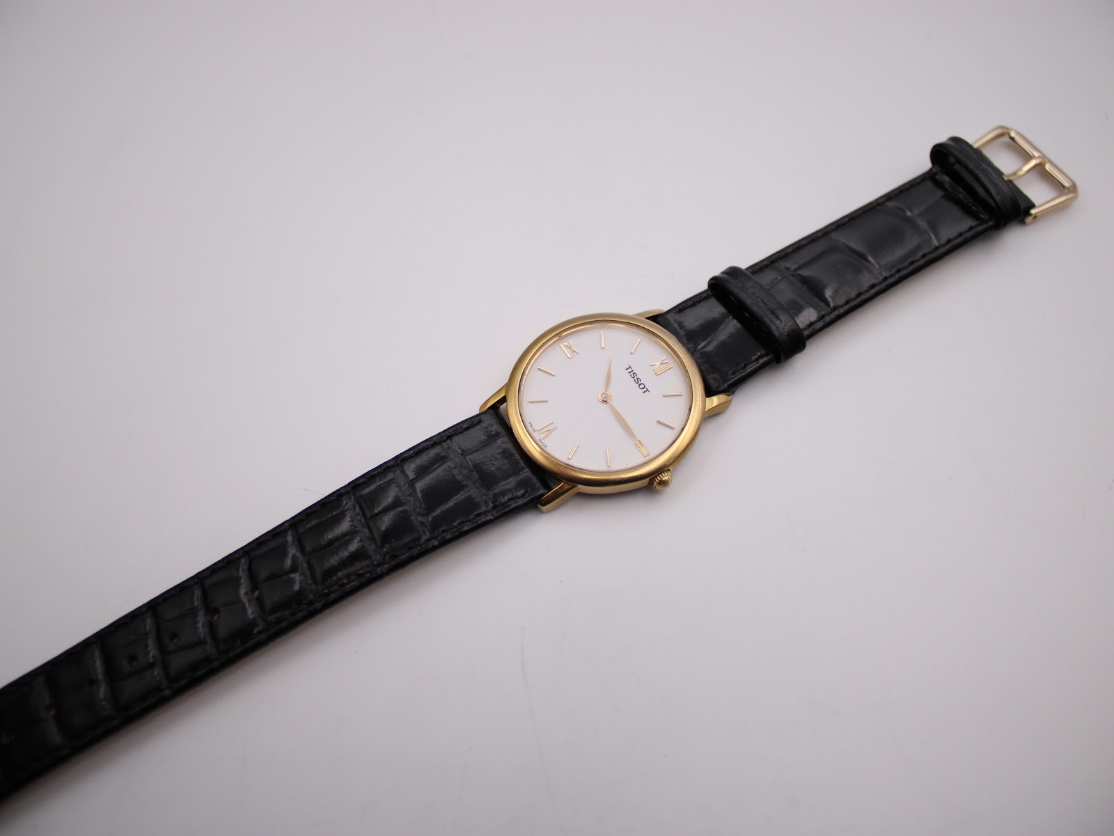 Full view of the Tissot watch from an angle, showing the entire black crocodile-grain leather strap and gold-tone buckle.