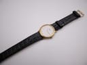 Full view of the Tissot watch from an angle, showing the entire black crocodile-grain leather strap and gold-tone buckle.