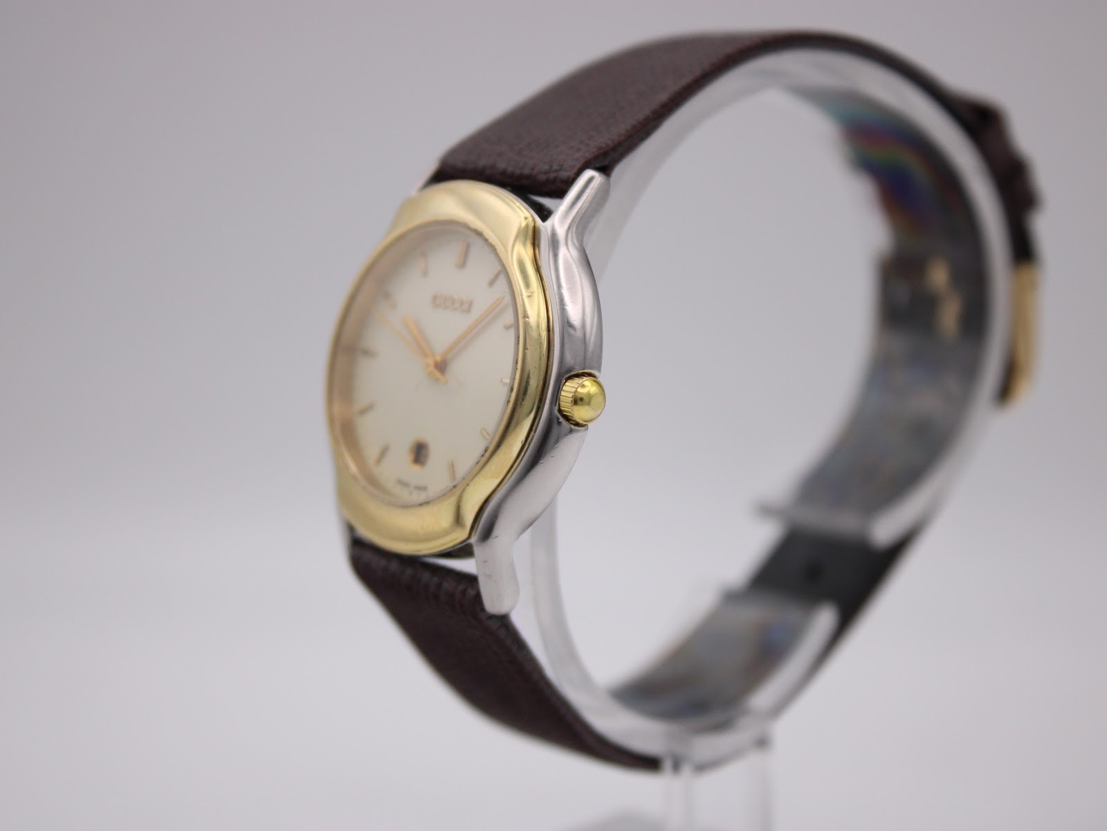 Angled side view of the Gucci watch, showing the polished gold-plated bezel and stainless steel case with the crown.