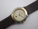 High-angle view of the Gucci watch dial, showcasing the cream face, gold hands, minimalist indices, and date window at 6 o'clock.