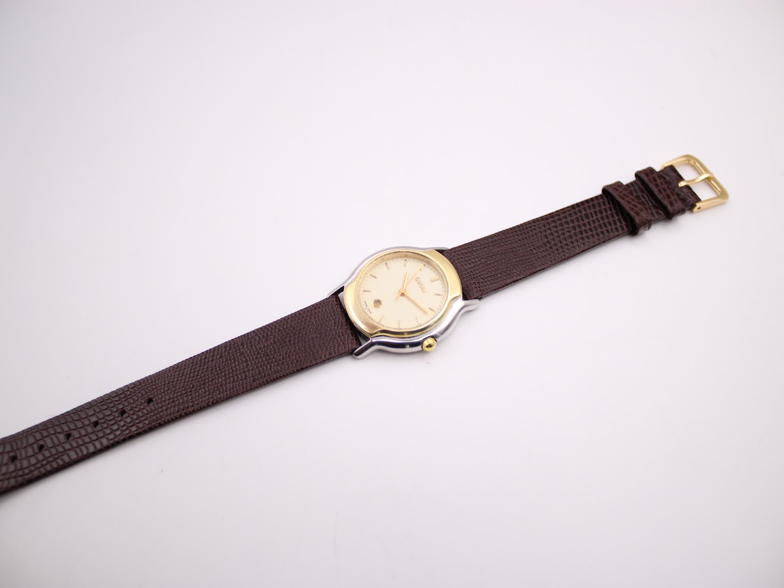Full length view of the Gucci watch on its brown textured leather strap with gold-tone buckle, laid flat.