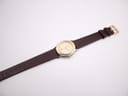 Full length view of the Gucci watch on its brown textured leather strap with gold-tone buckle, laid flat.