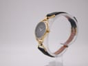 Side profile view of the Gucci watch on a stand, showing the round gold-tone case and crown.