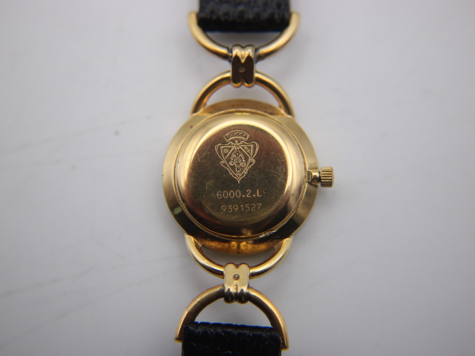 Close-up of the watch case back, revealing the Gucci crest, model number 6000.2.L, and serial number 9391527.