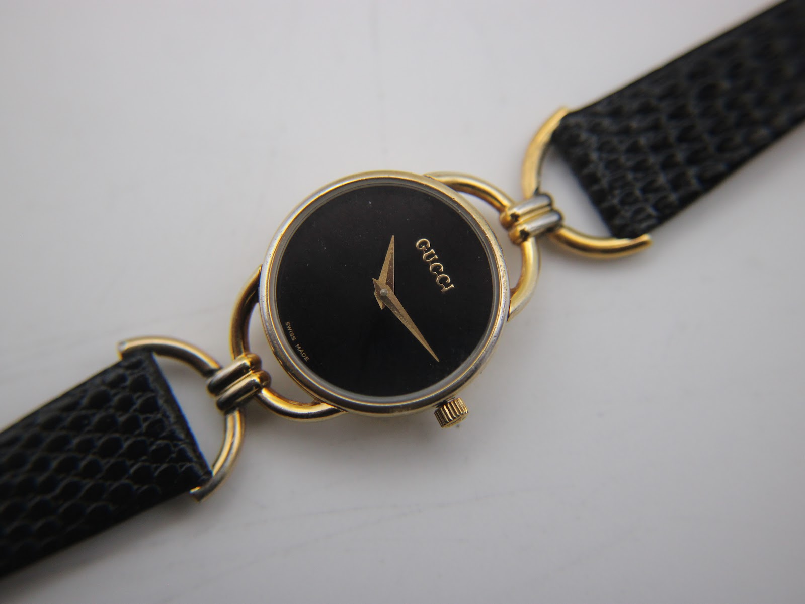 Overhead close-up of the black dial with gold-tone Gucci logo and hands, showing the texture of the black leather strap.