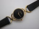 Overhead close-up of the black dial with gold-tone Gucci logo and hands, showing the texture of the black leather strap.