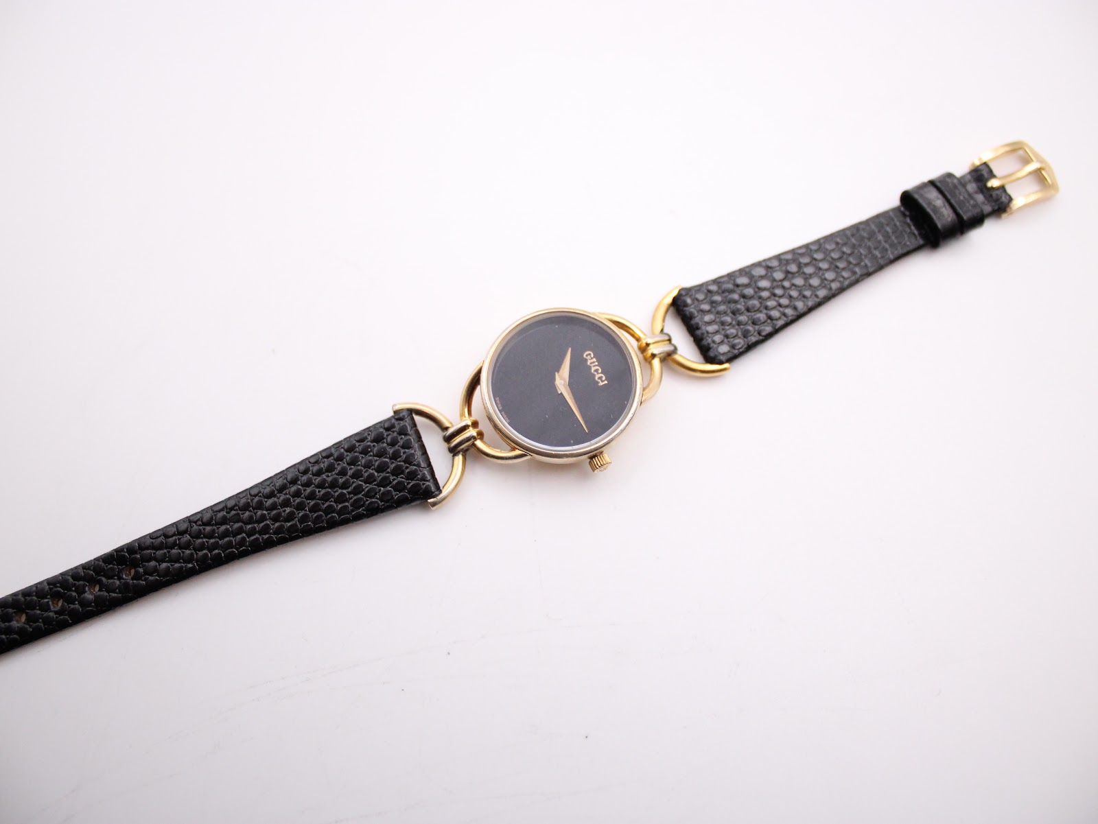 Full top-down view of the Gucci watch with its black textured leather strap extended on a white background.