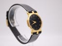 Opposite angled side view of the Gucci 3400M watch on a clear display stand, highlighting the gold case and black strap.