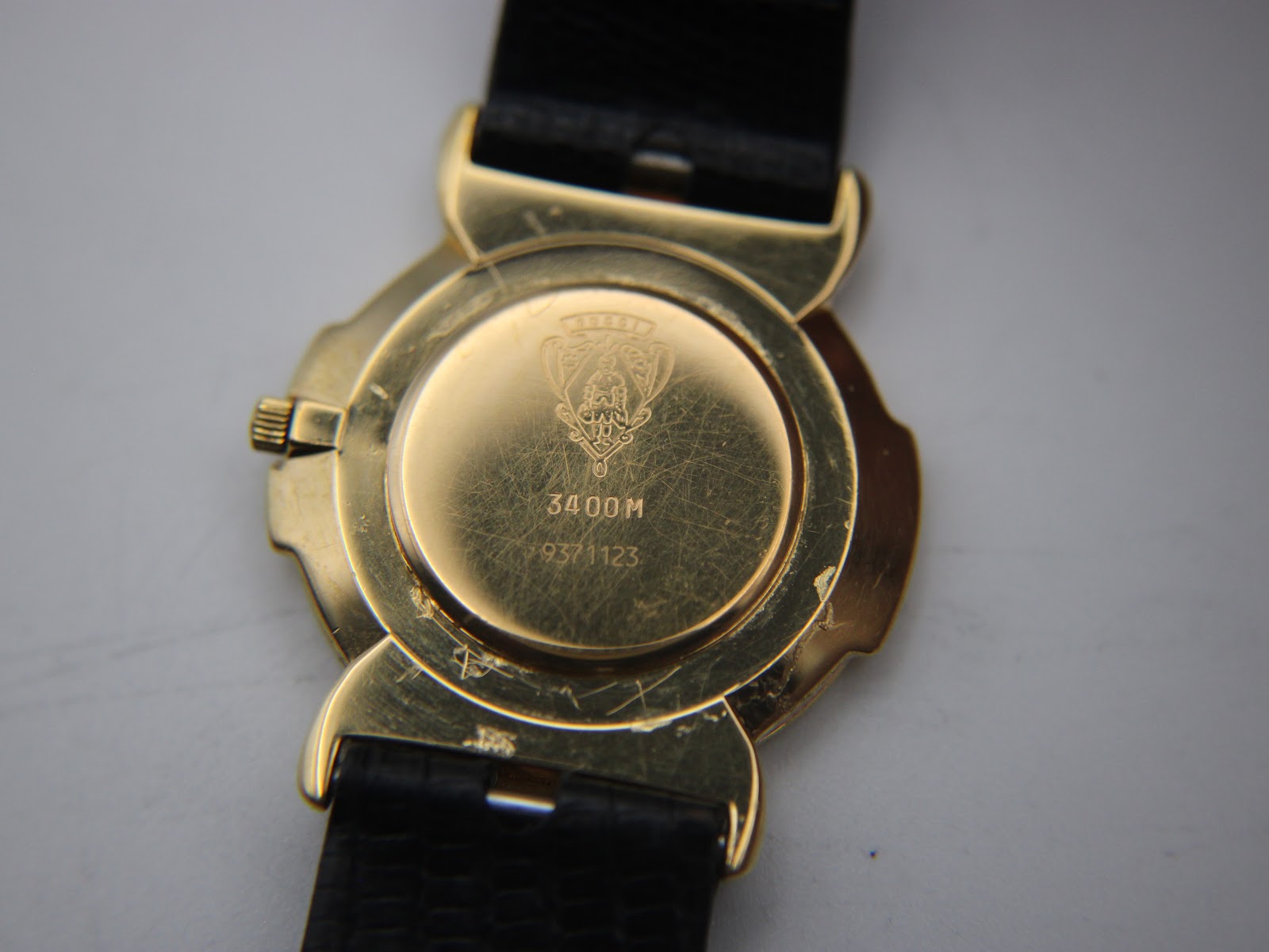 Close-up of the gold-plated case back of the Gucci 3400M, showing the Gucci crest, model number 3400M, and serial number 9371123, with visible surface scratches.