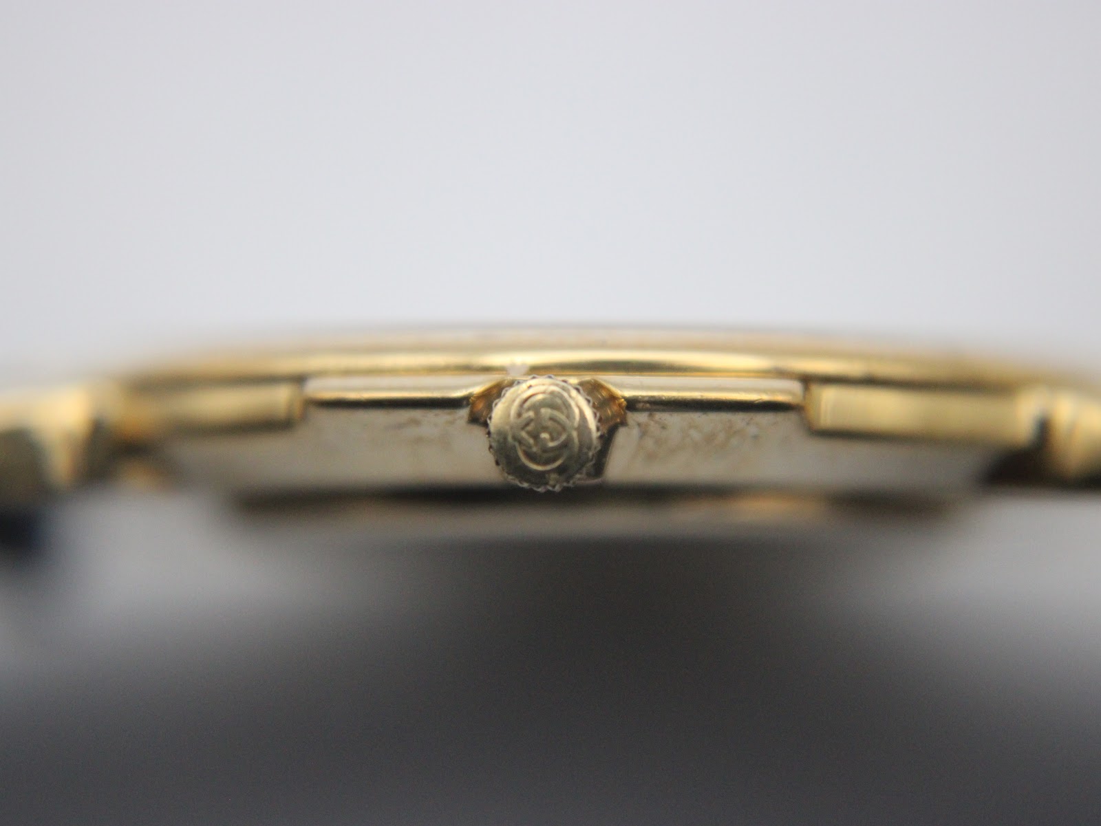 Macro close-up of the side of the watch case, focusing on the gold-tone crown embossed with the Gucci interlocking Gs logo.