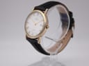 Angled side view of the Bulova watch, showing the gold-tone bezel and black leather strap on a stand.
