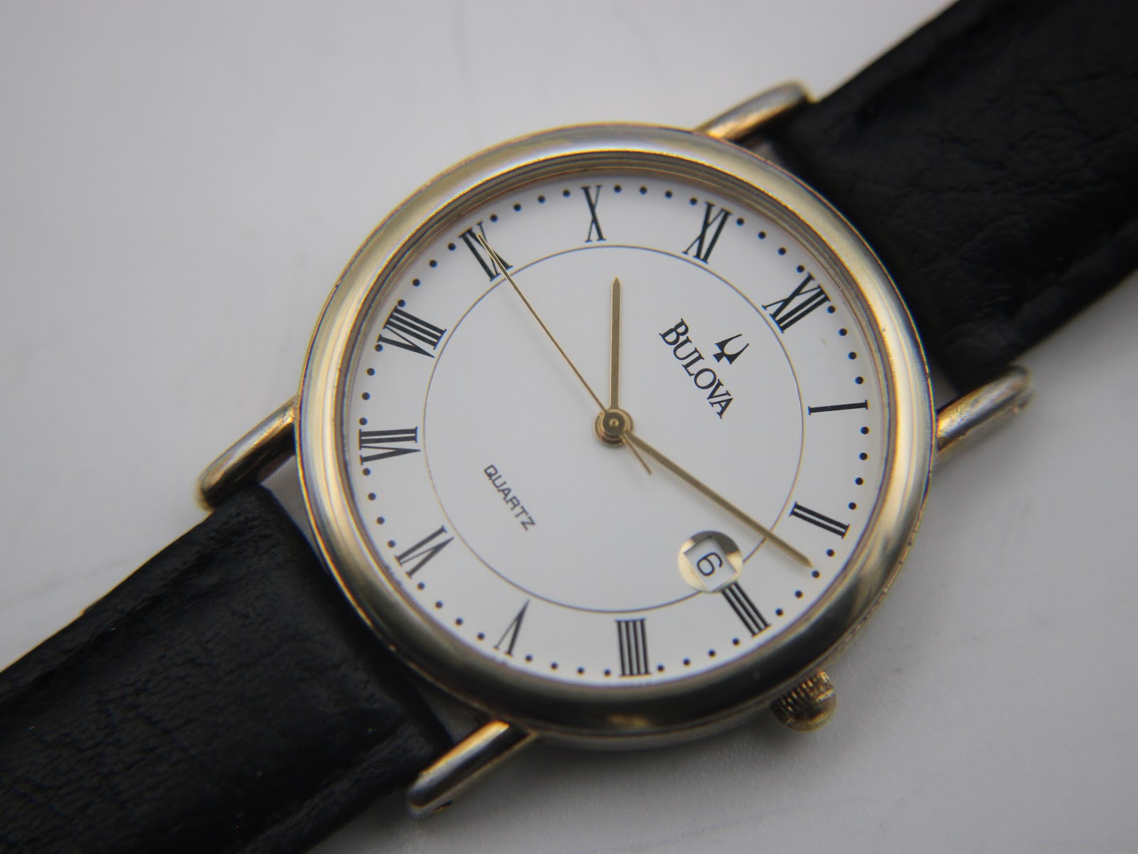 Detailed close-up of the white dial with black Roman numerals, gold-tone hands, and date window.