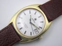 Close-up of the silver dial, showing the vertically brushed texture, applied gold baton indices, and date window.
