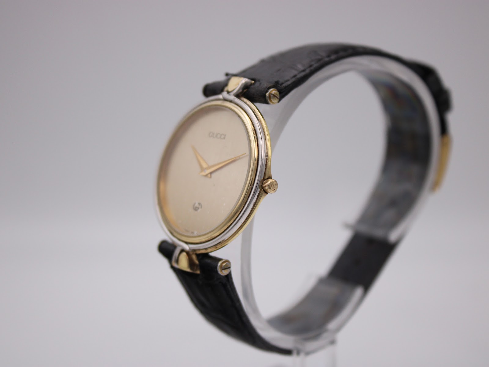 Angled side view of the Gucci 4500 M watch showing the profile of the two-tone case and the black leather strap.