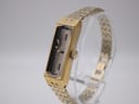 Side view of the gold-plated Seiko watch on a clear stand, highlighting the rectangular case and crown.