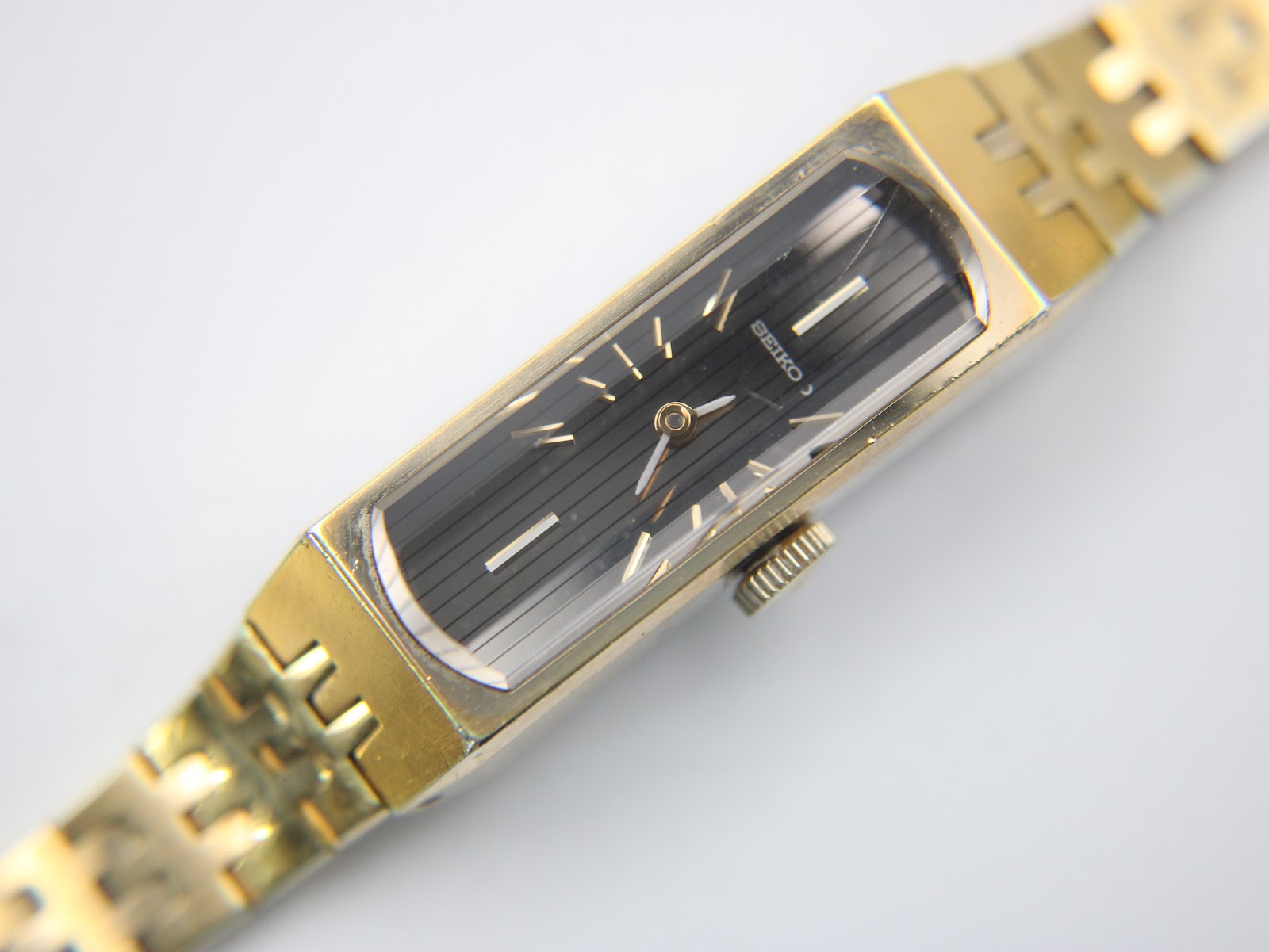 Angled close-up of the Seiko watch, focusing on the rectangular gold-plated case and the detailed black dial.