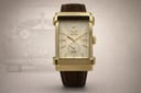 Front view of the XO RETRO Automotive DNA MCML watch, showing rectangular gold case, cream dial with small seconds sub-dial, and brown leather strap, with a ghosted classic car image in the background.