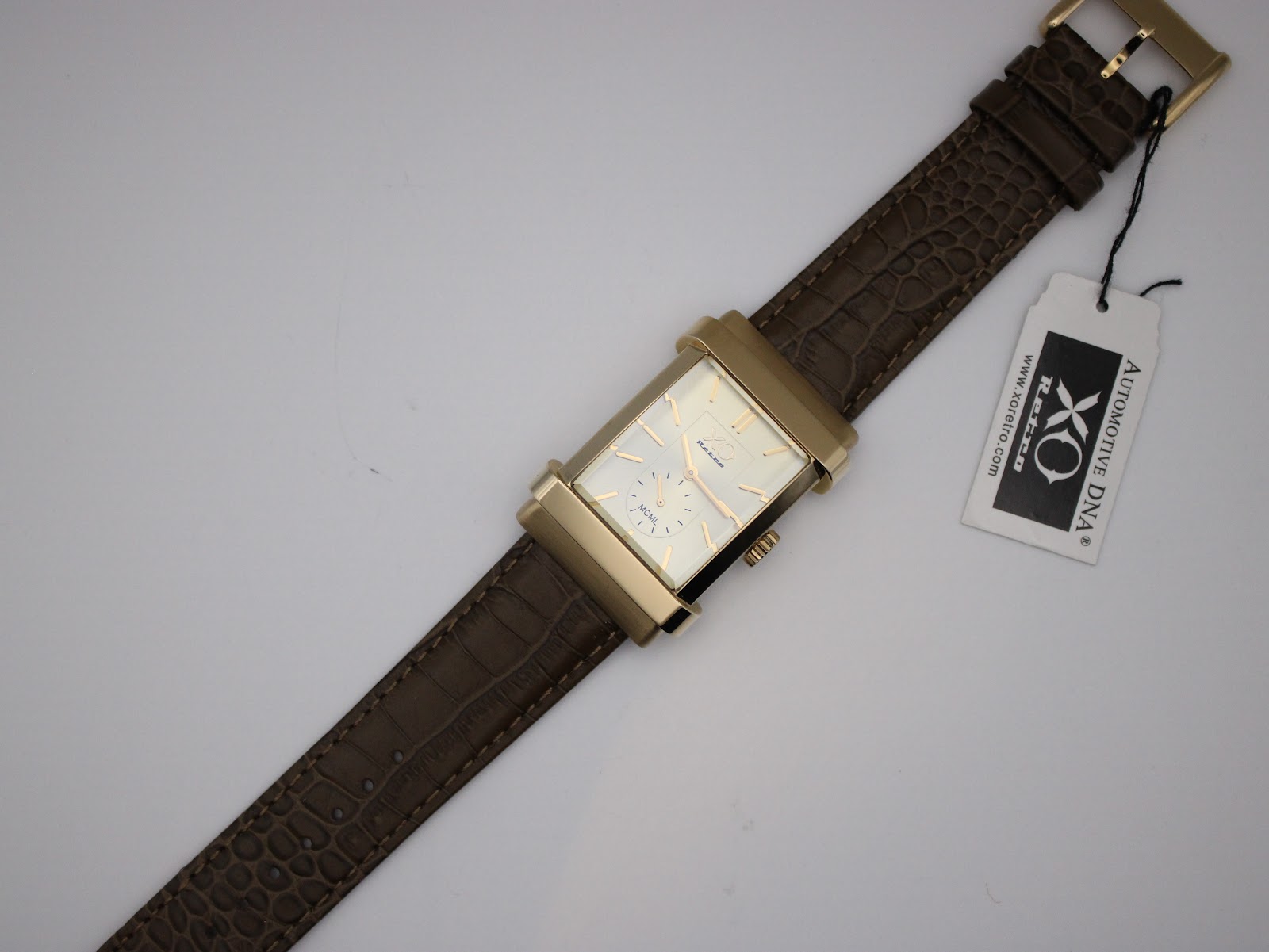 Overhead view of the XO RETRO watch, laid flat, showing the full brown crocodile-effect leather strap with a hang tag attached.