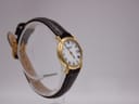 Another angled side view of the Raymond Weil watch, showing the dial, crown, and brown leather strap on a clear stand.