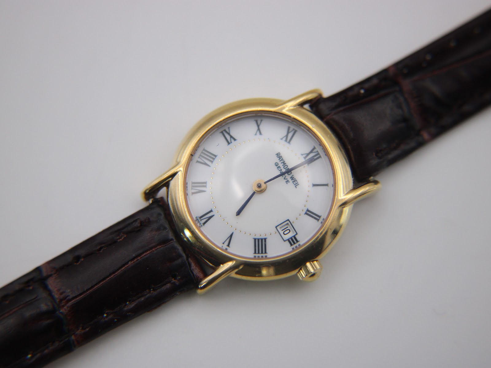 Top-down close-up of the Raymond Weil 9940 watch face, detailing the white dial, black Roman numerals, and date window at 3 o'clock.