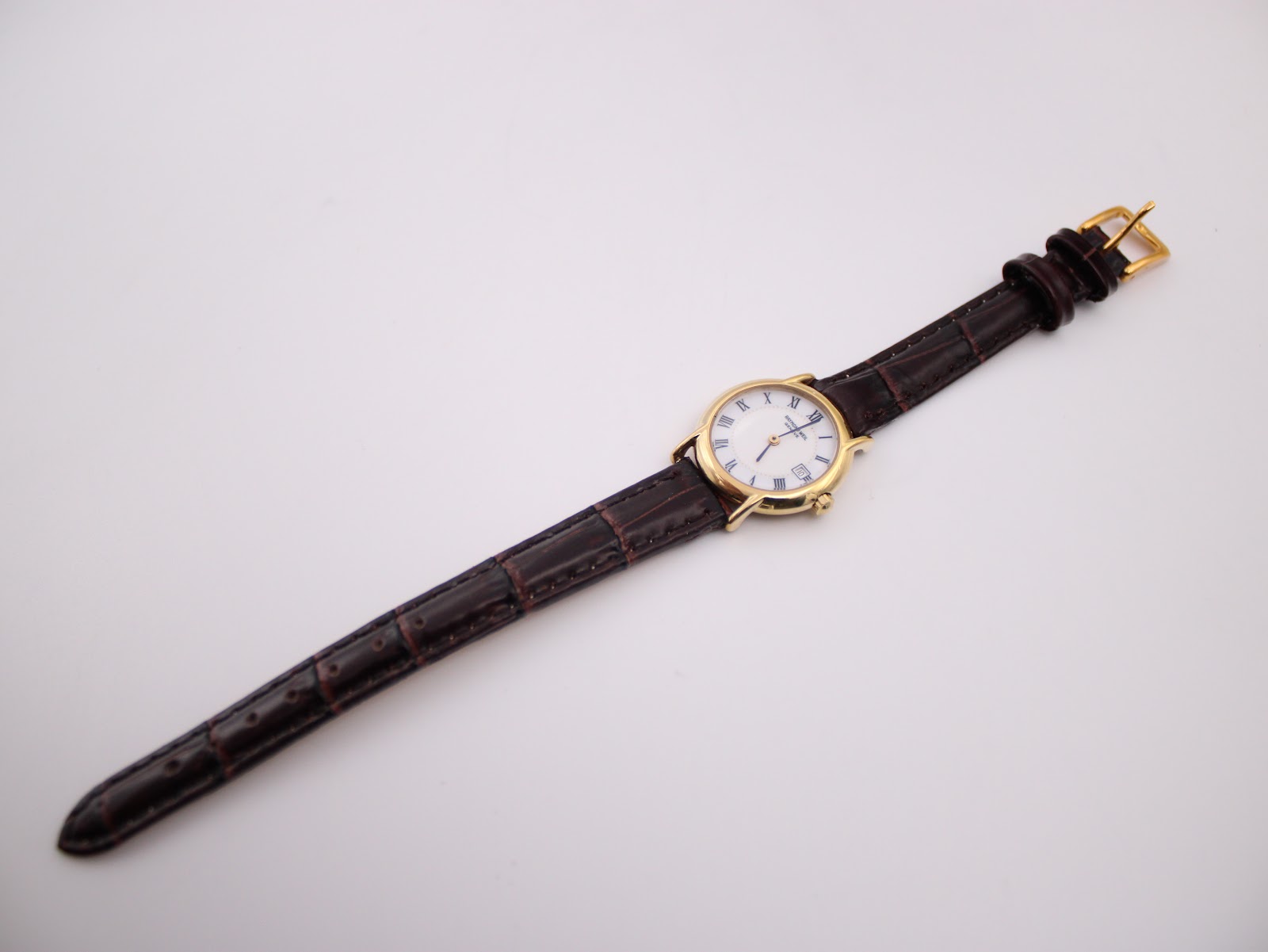 Full length top view of the Raymond Weil watch, showcasing the gold case and the crocodile-grain brown leather strap with a gold buckle.
